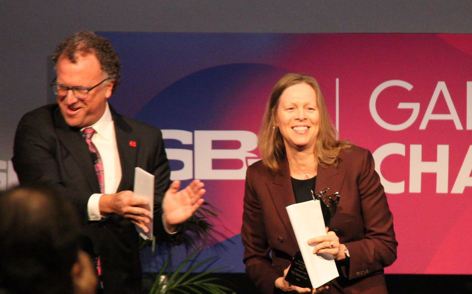Val Ackerman smiles holding her award on stage as Abe Madkour gestures beside her
