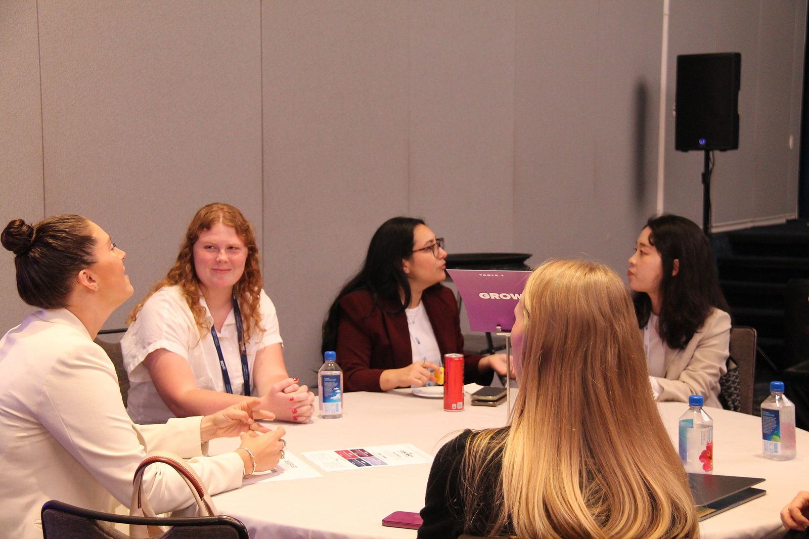Attendees talking at a round table with a purple Grow sign