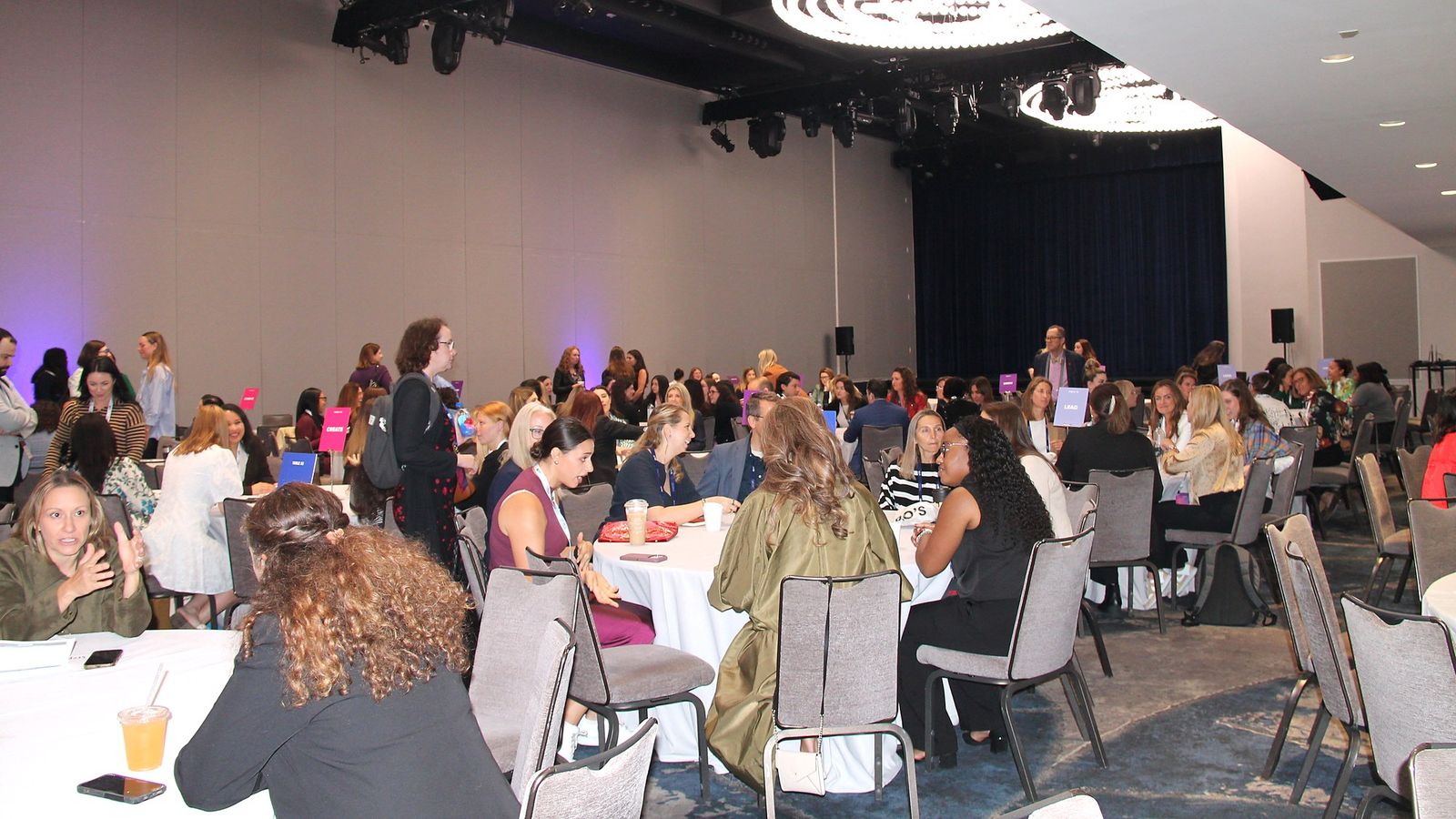 A ballroom full of attendees seated at round tables in conversation