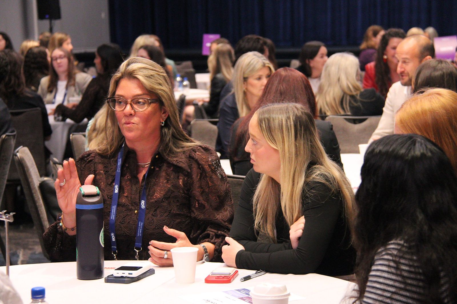 An attendee speaks with her hands at a table in the busy ballroom