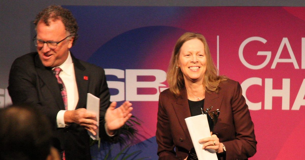 Val Ackerman smiles holding her award on stage as Abe Madkour gestures beside her
