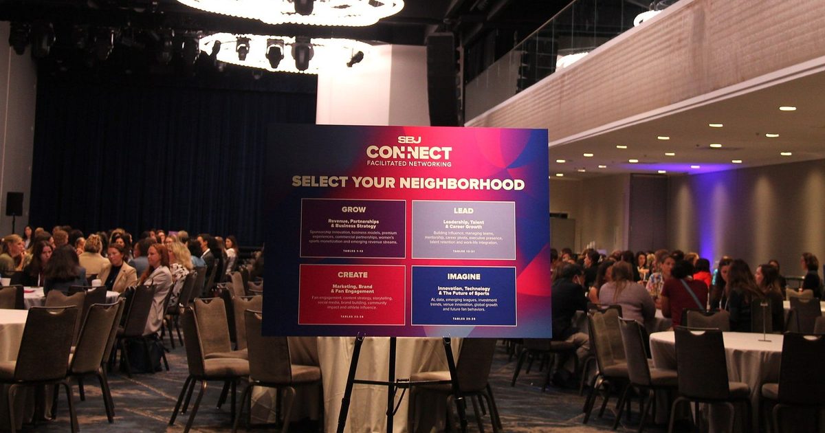 An easel sign reading SBJ Connect, Select Your Neighborhood, in front of a ballroom full of round tables