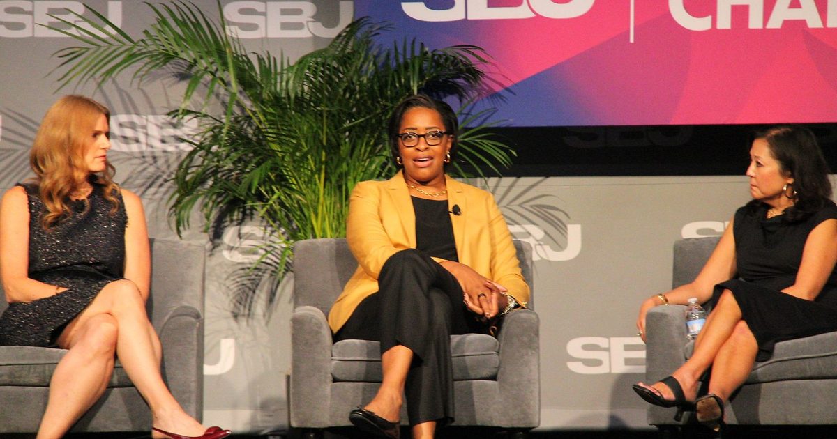 Three panelists seated on stage during the college athletics session