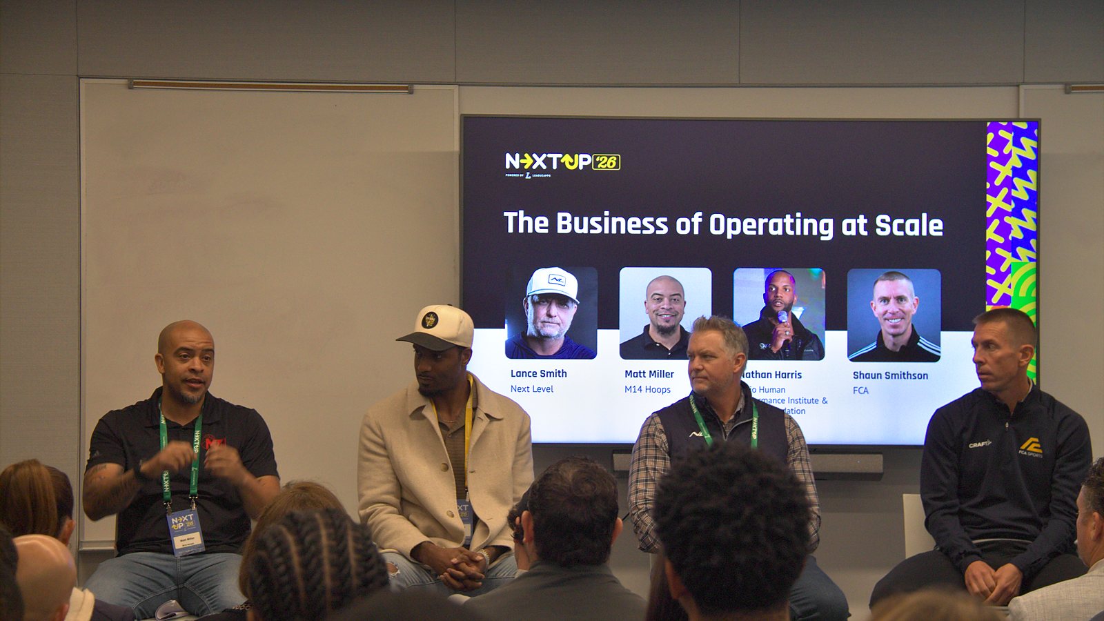 Matt Miller gestures while speaking, seated with Nathan Harris, Lance Smith and Shaun Smithson in front of a screen reading The Business of Operating at Scale