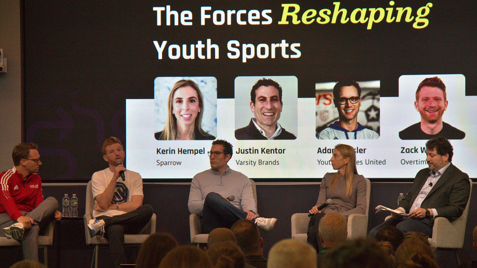 Five people seated on stage beneath a slide titled The Forces Reshaping Youth Sports